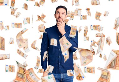 Elleri çenesinde gündelik tişört giyen genç ve yakışıklı bir adam soru sormayı düşünüyor, düşünceli bir ifade. Gülümseyen ve düşünceli bir yüz. şüphe kavramı.