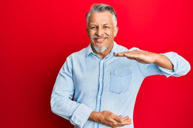 Orta yaşlı, gri saçlı, sıradan kıyafetler giyen, elleri büyük ve büyük boy işareti gösteren, ölçü sembolü olan bir adam. Kameraya bakıp gülümsüyor. ölçüm kavramı. 