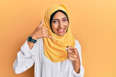 Genç esmer Arap kadın geleneksel İslami başörtüsü takıyor gülümsüyor telefonda konuşuyor ve seni işaret ediyor. Ara beni.. 