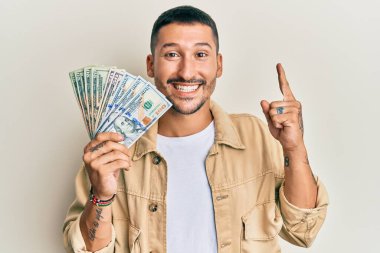 Dövmeleri olan yakışıklı bir adam elinde dolarlarla gülümseyen bir fikir ya da soru işareti yapan mutlu yüzlü bir adam. 