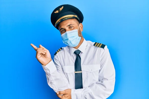 髭を生やしたハンサムな男は飛行機のパイロットの制服を着て安全マスク笑顔幸せなポインティングで手と指で側面に — ストック写真