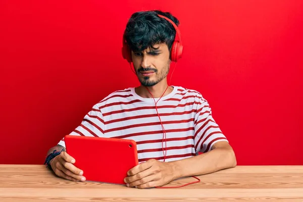 Junge Hispanische Mann Mit Touchpad Trägt Kopfhörer Ahnungslos Und Verwirrt — Stockfoto