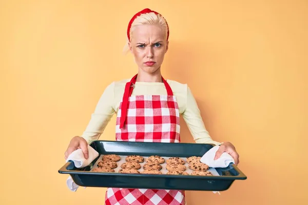 Mujer Rubia Joven Con Uniforme Panadero Sosteniendo Galletas Caseras Escéptico —  Fotos de Stock