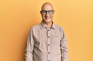 Yüzünde mutlu ve havalı bir gülümsemeyle orta yaşlı kel bir adam günlük kıyafetler ve gözlük takıyor. şanslı kişi. 