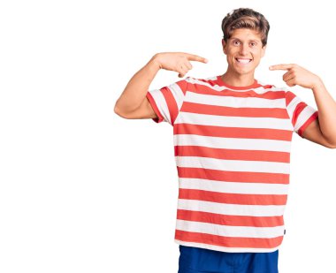 Gündelik kıyafetler giyen, neşeli gülümseyen, parmaklarıyla ve ağzıyla işaret eden genç yakışıklı bir adam. diş sağlığı kavramı. 