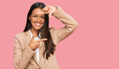 Güzel İspanyol kadın iş ceketi giyip gülümsüyor ve mutlu yüzlü eller ve parmaklarla çerçeve yapıyor. yaratıcılık ve fotoğrafçılık kavramı. 