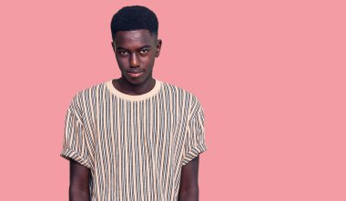 Afro-Amerikalı genç bir adam günlük kıyafetler giyip ellerinin birarada dua ederek af diliyor kendinden emin bir şekilde gülümseyerek. 