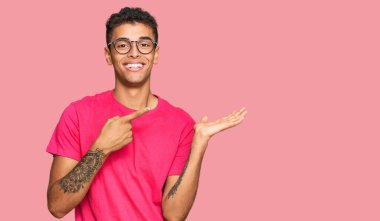 Genç, yakışıklı, Afro-Amerikalı sıradan kıyafetler giyen adam kameraya hayret ediyor ve gülümsüyor.. 