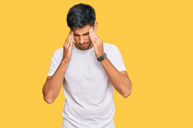 Genç ve yakışıklı bir adam, stresten dolayı başı ağrıyan günlük beyaz tişörtler giyiyor. migren ağrısı. 