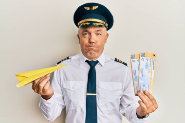 Yakışıklı, olgun bir pilot elinde kağıt uçak ve komik suratlı, şişirilmiş yanaklar tutuyor. Ağzı havayla şişer, havayı yakalar.. 