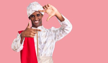 Geleneksel Sherwani sari giysileri giyen Afrikalı yakışıklı bir adam gülümseyerek elleri ve parmakları gülen yüzlü bir çerçeve yapıyor. yaratıcılık ve fotoğrafçılık kavramı. 