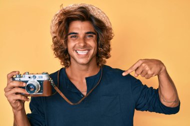 Şapkalı genç İspanyol adam, elinde antika kamerayla gülümseyen mutlu ve gururlu birini işaret ediyor. 