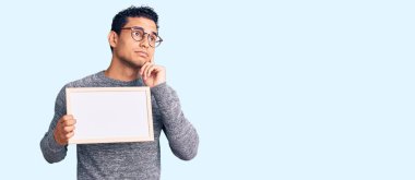 İspanyol yakışıklı genç adam boş afiş tutuyor ciddi bir yüz soru soruyor çene üstüne çene, kafa karıştırıcı fikir hakkında düşünceli. 