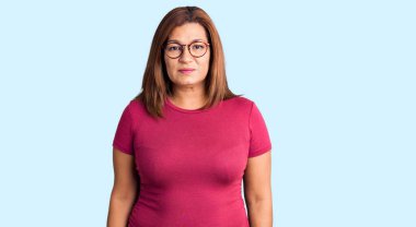 Orta yaşlı Latin kadın günlük kıyafetler giyiyor ve yüzünde ciddi bir ifade olan gözlük takıyor. Basit ve doğal bir şekilde kameraya bakıyorsun.. 