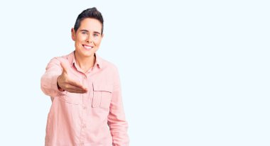 Kısa saçlı, günlük kıyafetler giyen, samimi bir şekilde el sıkışarak selamlaşan genç bir kadın. başarılı iş. 