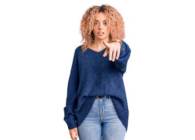 Kış süveteri giyen kıvırcık saçlı genç sarışın kadın kameraya kızgın ve sinirli bir şekilde bakıyor. 