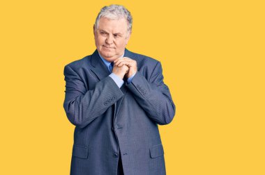 İş ceketi giyen yaşlı gri saçlı adam elleri çenesinde gergin ve heyecanlı bir şekilde yan tarafa bakıyor. 
