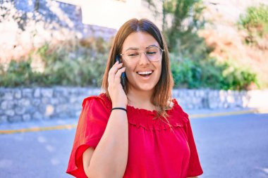 Genç ve güzel bir kadın rahat bir elbise ve mutlu bir gülümseme takınıyor. Yüzünde gülümsemeyle şehrin caddesindeki akıllı telefondan konuşarak..