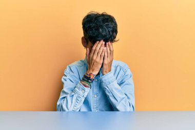 Latin asıllı genç adam, gündelik giysiler içinde masaya oturmuş ağlarken suratını ellerle kapatıyor. depresyon kavramı. 