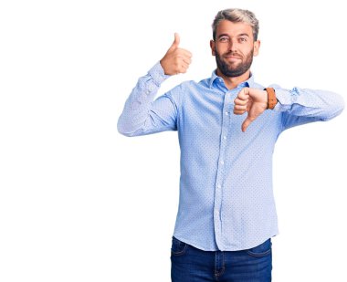 Zarif tişört giyen genç, sarışın bir adam baş parmaklarını yukarı aşağı hareket ettiriyor, anlaşmazlık ve uzlaşma ifadesi. çılgın çatışma 