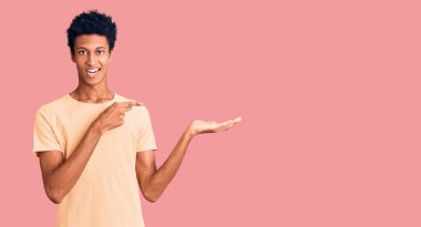 Genç Afro-Amerikalı sıradan kıyafetler giyen adam kameraya hayret ediyor ve gülümsüyor.. 