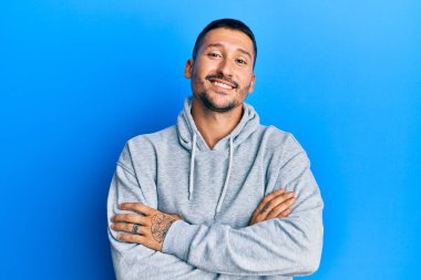 Kollarını kavuşturup kameraya bakan, sıradan, mutlu yüzlü dövmeli yakışıklı bir adam. pozitif kişi. 