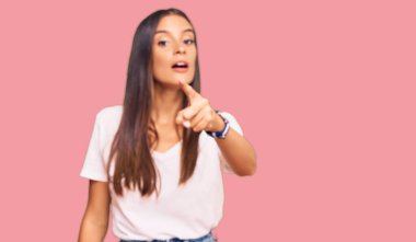 Gündelik beyaz tişört giyen genç İspanyol kadın kameraya kızgın ve sinirli bir şekilde seni işaret ediyor. 