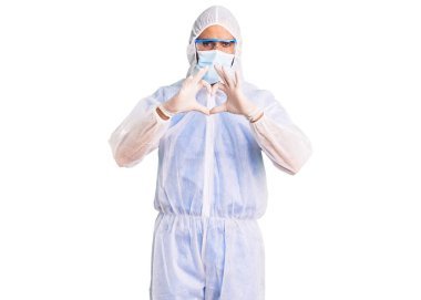 Koronavirüs üniforması giyen genç İspanyol bir adam ve elleri ile kalp sembolü şeklinde gülümseyen bir tıbbi maske. romantik kavram. 