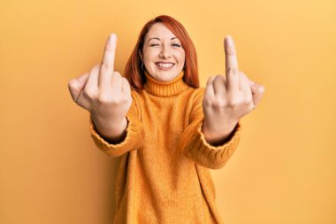 Güzel kızıl saçlı kadın orta parmağını gösteriyor. Kötü jest yapıyor. Seksi bir ifadeyle kameraya bakıyor.. 