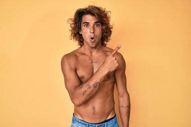 Genç, İspanyol asıllı, tişörtsüz bir adam parmağını yana doğru kaldırmış, ağzı açık, şaşkın bir ifade sergiliyor.. 