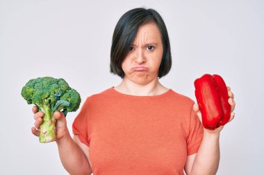 Down sendromlu esmer kadın elinde brokoli ve kırmızı biber tutuyordu. Depresyondaydı ve sıkıntıdan endişe ediyordu. Öfkeli ve korkmuştu. hüzünlü ifade. 