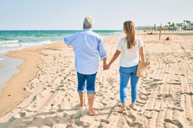 Orta yaşlı İspanyol bir çift sahilde arka planda yürüyor..