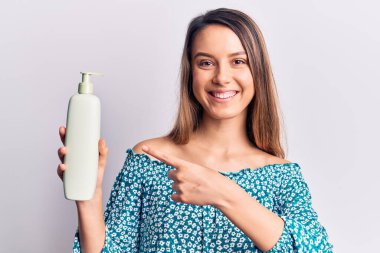 Genç, güzel bir kız elinde krem losyon şişesiyle gülümsüyor. 
