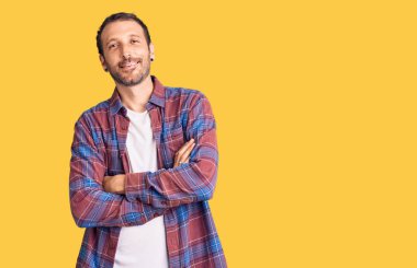 Sıradan kıyafetler giyen, kollarını kavuşturup kameraya bakan mutlu yüzlü genç bir adam. pozitif kişi. 