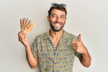 500 Norveç kronu taşıyan sakallı yakışıklı adam mutlu ve olumlu gülümsüyor, başparmağıyla mükemmel ve onay işareti yapıyor. 