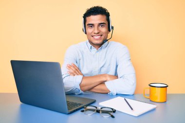 Young handsome hispanic man working at the office wearing operator headset happy face smiling with crossed arms looking at the camera. positive person.  clipart