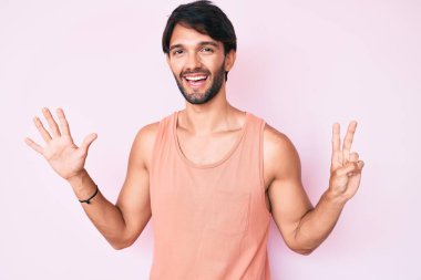 Yakışıklı İspanyol adam gündelik giysiler giyip yedi numarayı gösterip işaret ederken kendinden emin ve mutlu gülümsüyor.. 