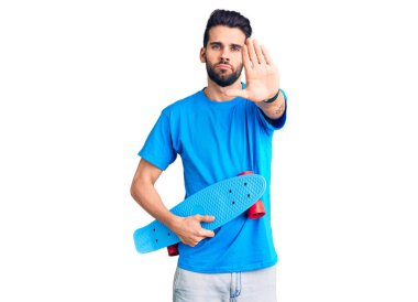 Young handsome man with beard holding skate with open hand doing stop sign with serious and confident expression, defense gesture 