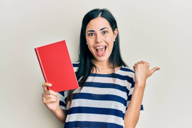 Güzel, genç bir kadın kitap okuyor başparmağıyla yan tarafa bakıyor mutlu bir şekilde ağzı açık gülümsüyor. 