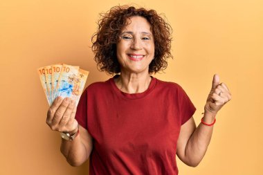 Güzel orta yaşlı bir kadın elinde 10 İsviçre frangı banknotuyla gururla bağırıyor zaferi ve başarıyı kutluyor. 