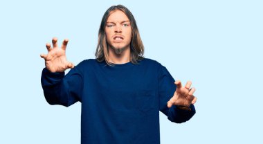 Handsome caucasian man with long hair wearing casual winter sweater smiling funny doing claw gesture as cat, aggressive and sexy expression 