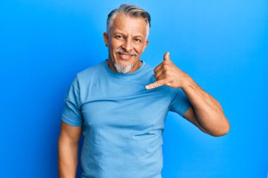 Orta yaşlı, gri saçlı, günlük kıyafetler giyen, gülümseyen, el ve parmaklarıyla telefonla konuşan bir adam. iletişim kavramları. 