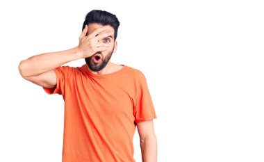 Sakallı, sıradan tişörtler giyen, yüzü ve gözleri kapalı, utangaç ifadesiyle parmaklarının arasından bakan genç yakışıklı bir adam.. 