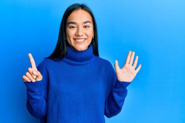 Genç Asyalı kadın, günlük kışlık süveter giyer ve altı numaralı parmaklarıyla gülümseyerek mutlu ve kendinden emin bir şekilde onu işaret eder.. 