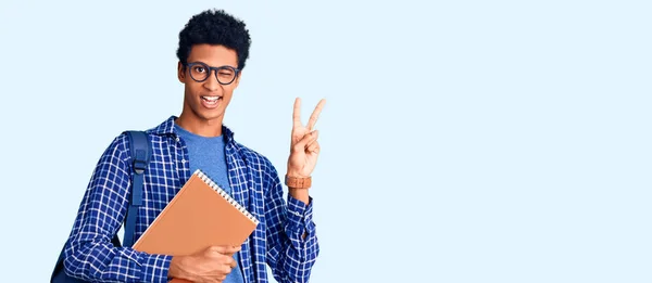 年轻的非洲裔美国人 背着学生背包 拿着书本 喜形于色地微笑着 用手指拍着胜利的标志 第二点 — 图库照片