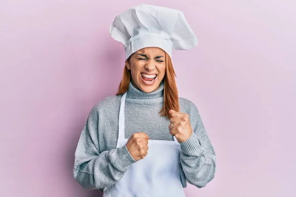 身穿职业厨师制服 头戴帽子的西班牙裔年轻女性惊讶地举起双臂 闭上眼睛 庆祝胜利 — 图库照片