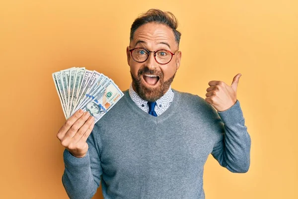 Handsome Middle Age Man Holding Dollars Pointing Thumb Side Smiling — ストック写真