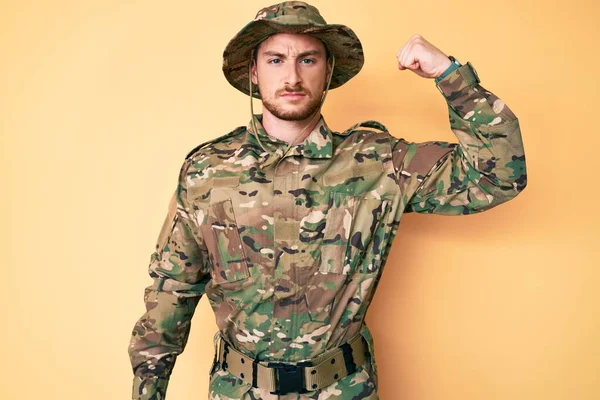 Young caucasian man wearing camouflage army uniform strong person showing arm muscle, confident and proud of power