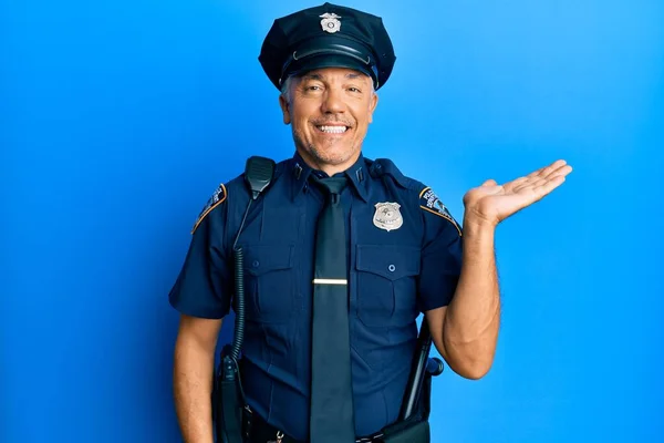 Handsome middle age mature man wearing police uniform smiling cheerful presenting and pointing with palm of hand looking at the camera.