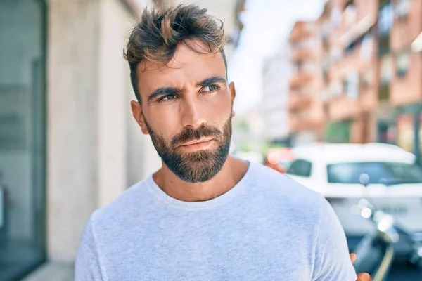 Young hispanic man with serious expression walking at the city